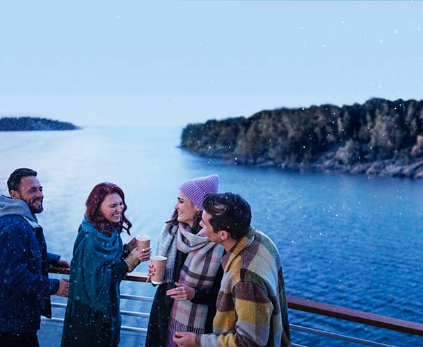Vänner står på utedäck med skärgården som bakgrund